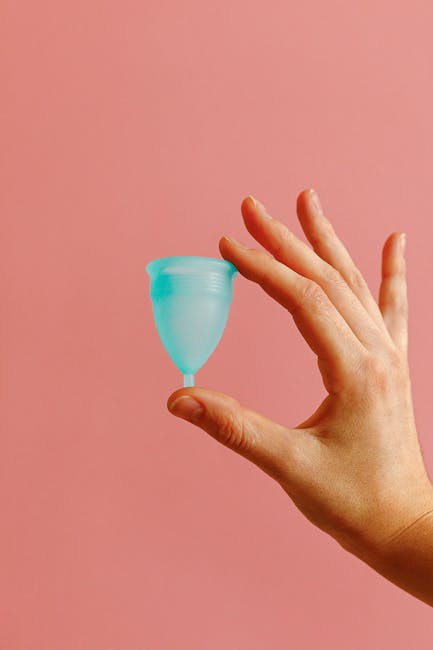 A reusable menstrual cup in a hand against a soft pink background, promoting eco-friendly feminine hygiene.